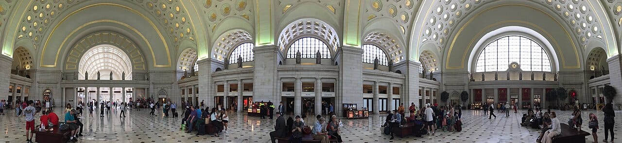 Panoramic view of the inside of Union Station's Great Hall. It is ornate with marble floors, and people inside are dwarfed by the 96 foot tall arched ceiling.